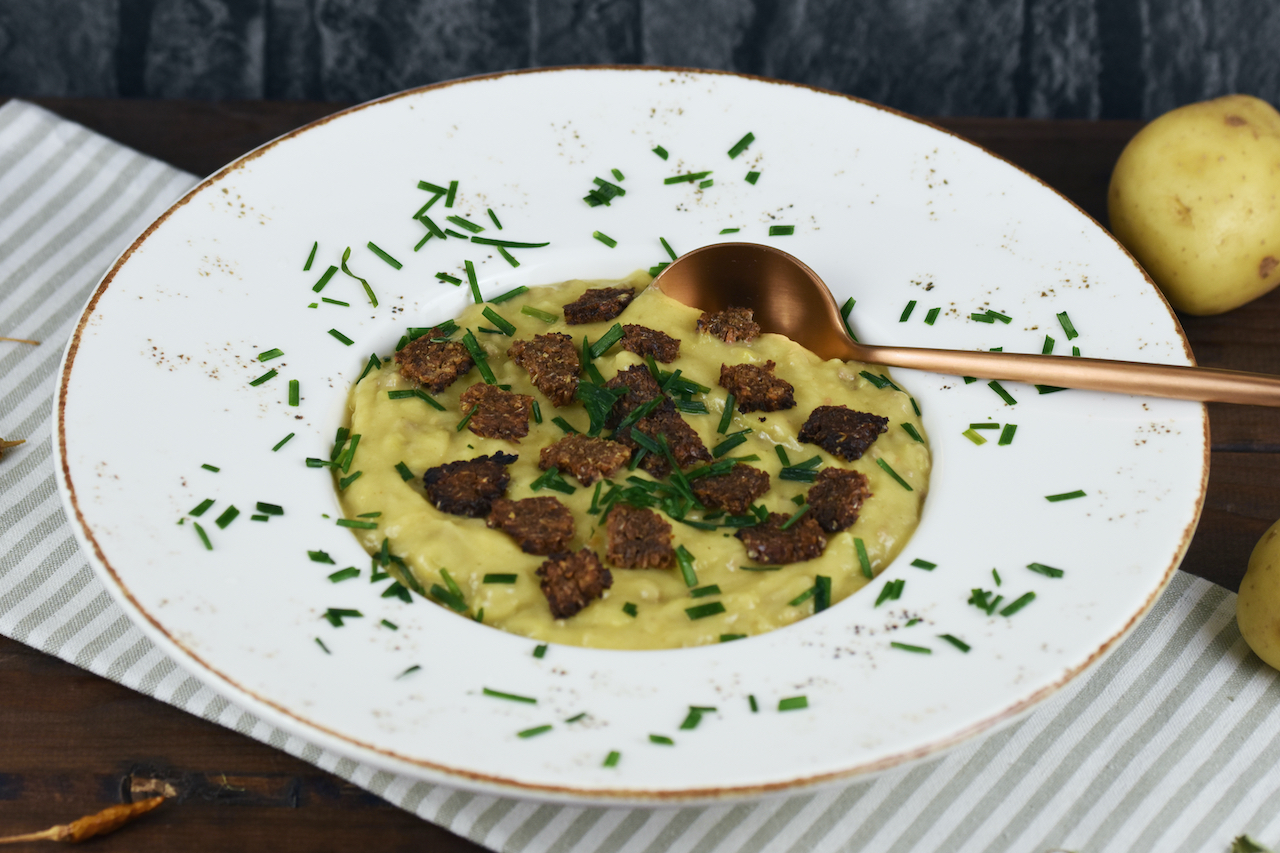 Cremige Kartoffel-Lauch-Suppe in einem weißen tiefen Teller. Hintergrund dunkel.