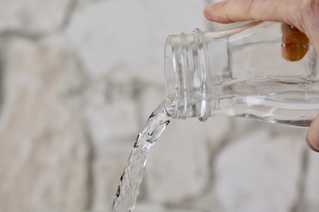Wasser wird aus einer Glasflsche geschüttet. Hintergrund hell.