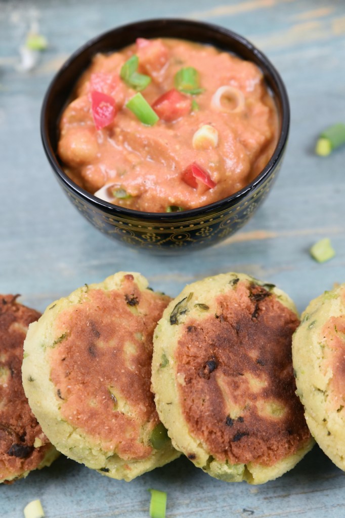 Indische Kartoffelküchlein auf blauem Teller. Dahinter steht eine Schale mit Kichererbsen-Curry.