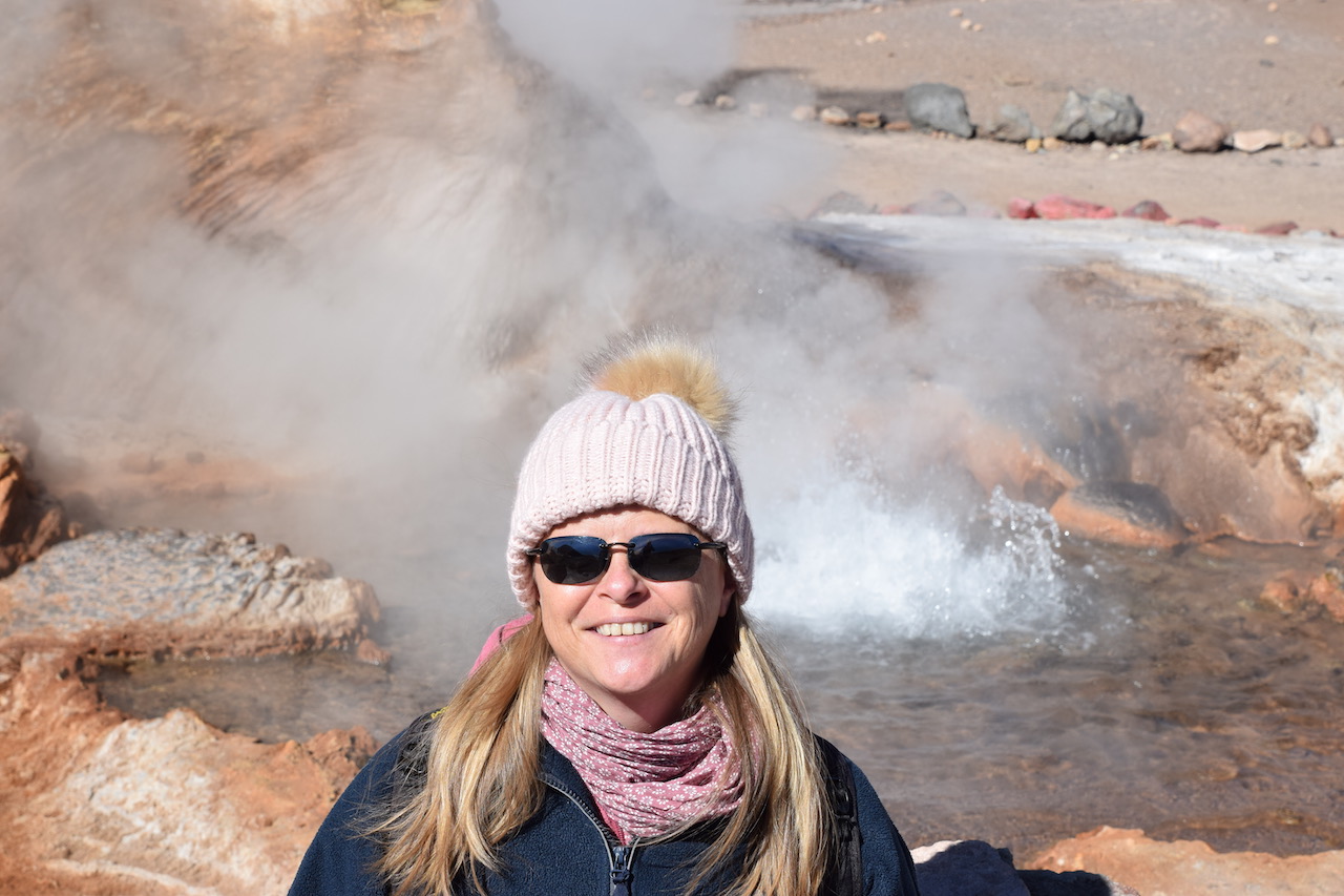 Über mich - Ich mit Mütze. Im Hintergrund sind ein Geysir und hellbraune Felsen