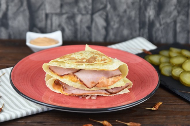 Reuben Sandwich-Tortilla Wrap auf rotem Teller. Hintergrund dunkel.