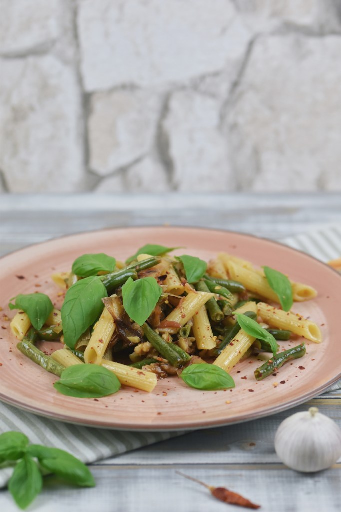 Zitronenpasta mit grünen Bohnen und Walnüssen auf einem rosa Teller.
