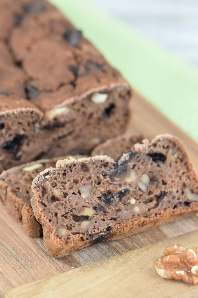 Angeschnittenes Bananenbrot mit Schokolade und Walnüssen auf Holzbrett. Hintergrund hell.
