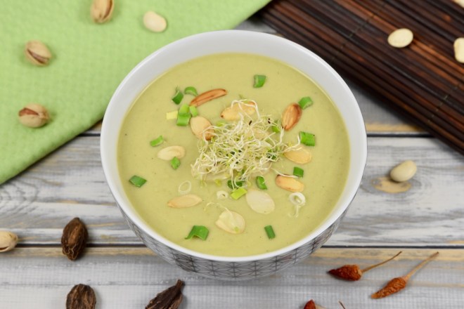 Schnelle Erbsensuppe in Porzellanschale, garniert mit Mandelplättchen, Frühlingszwiebeln und Sprossen. Hintergrund hell.