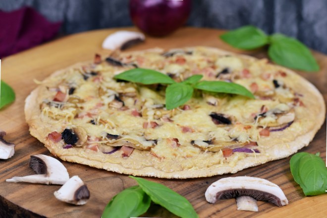 Veganer Flammkuchen mit Champignons und Basilikum auf Holzbrett.