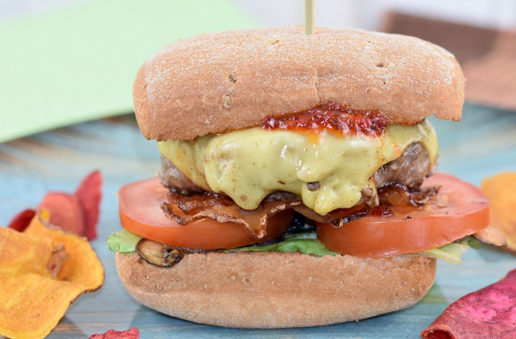 American Burger mit saftigem Rindfleisch-Patty auf blauem Teller. Hintergrund hell.