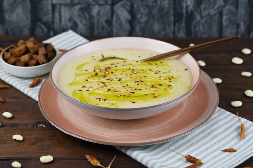 Cremige Blumenkohlsuppe in einem rosa Teller. Im Hintergrund stehen die Croûtons.