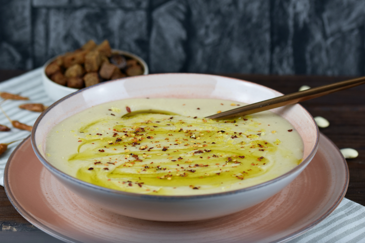 Cremige Blumenkohlsuppe in einem rosa Teller. Im Hintergrund stehen die Croûtons.