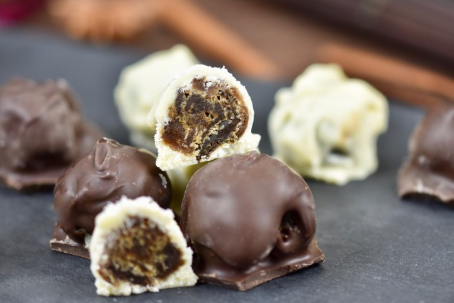 Lakto-Steinpilz-Pralinen mit weißem und dunklem Schokoüberzug auf Schieferplatte. Eine weiße Praline ist aufgeschnitten. Hintergrund dunkel