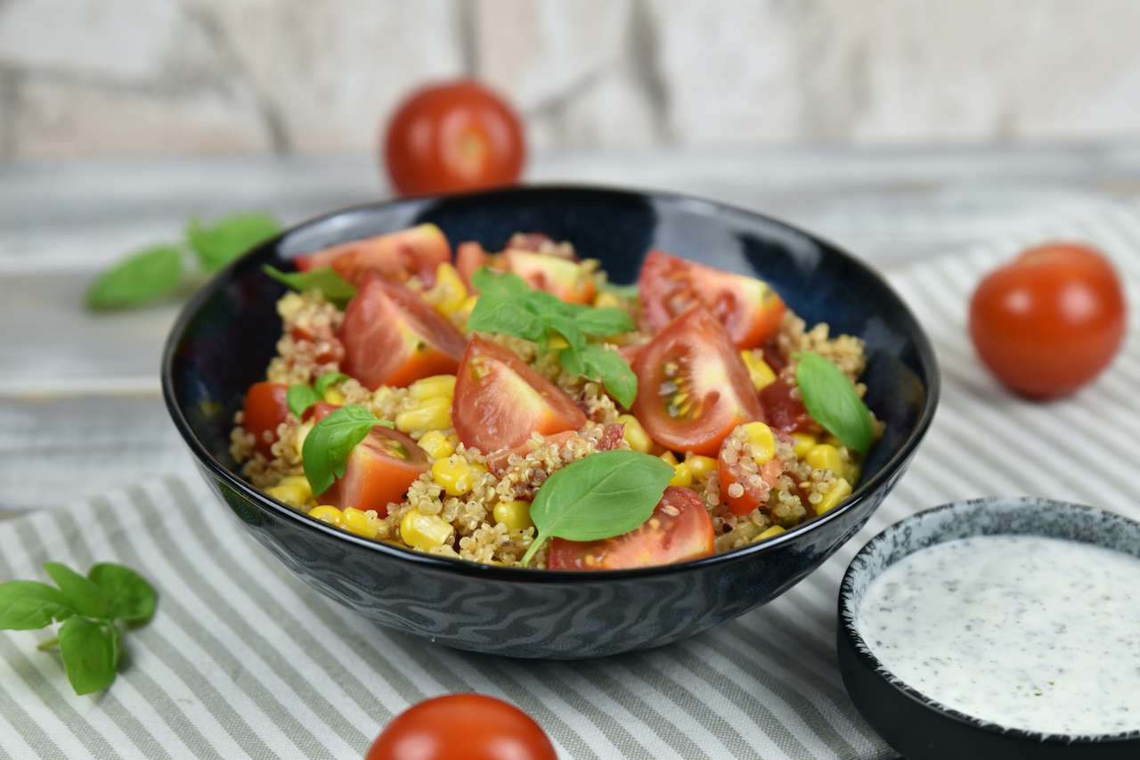 Quinoa Salat mit Avocado in einer schwarzen Schale. Daneben steht in einer kleineren Schale der Minz-Joghurt.