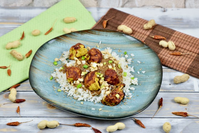 Knusprige Blumenkohlröschen mit Erdnusssauce und Reis, garniert mit Erdnüssen und Frühlingszwiebeln.