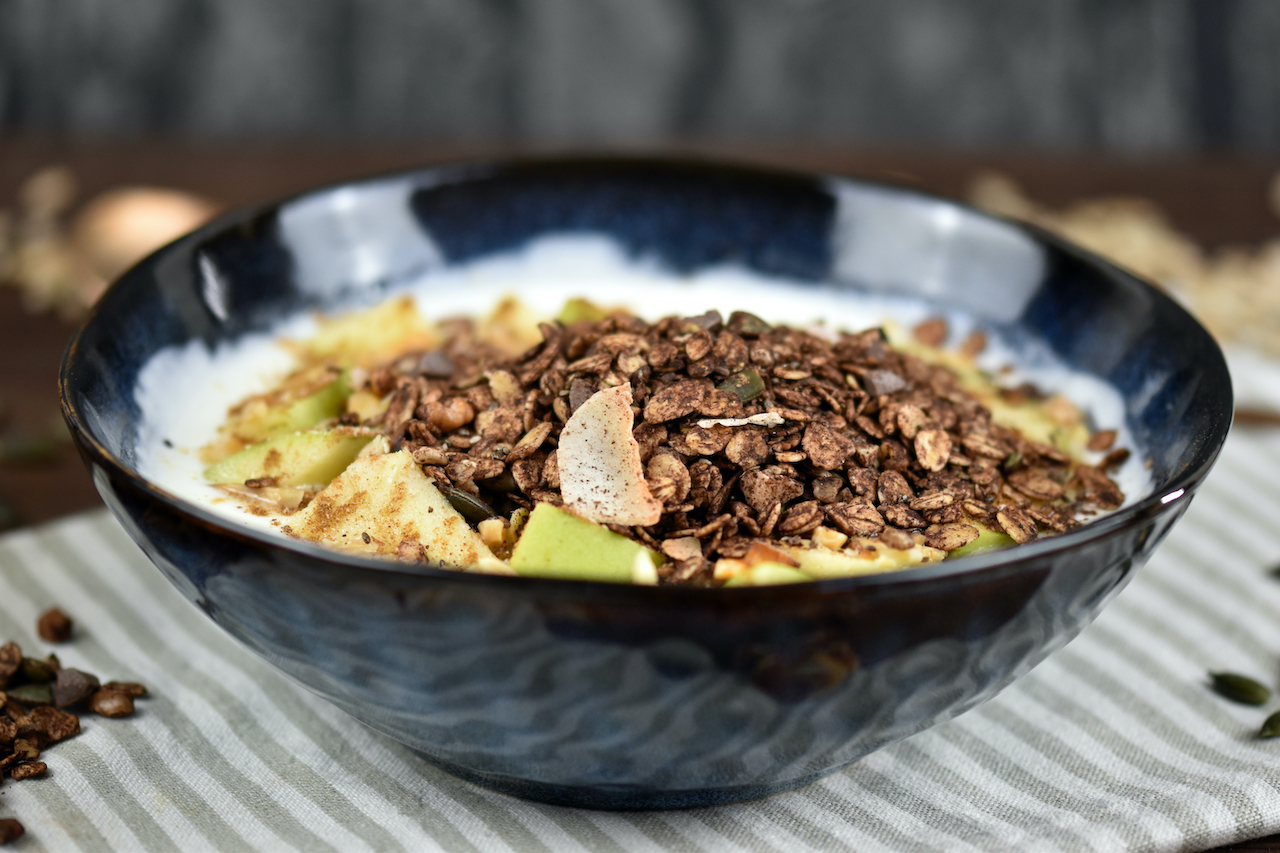 Schokoladen Granola in einer Schüssel mit Joghurt und Äpfeln.