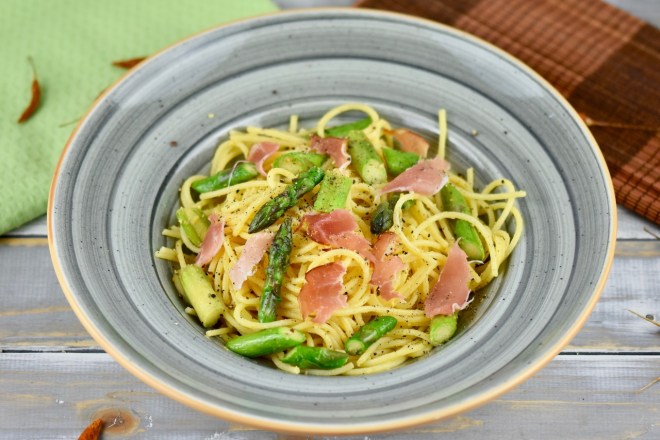 Orangen-Nudeln mit grünem Spargel in einem grauen tiefen Teller. Hintergrund hell.