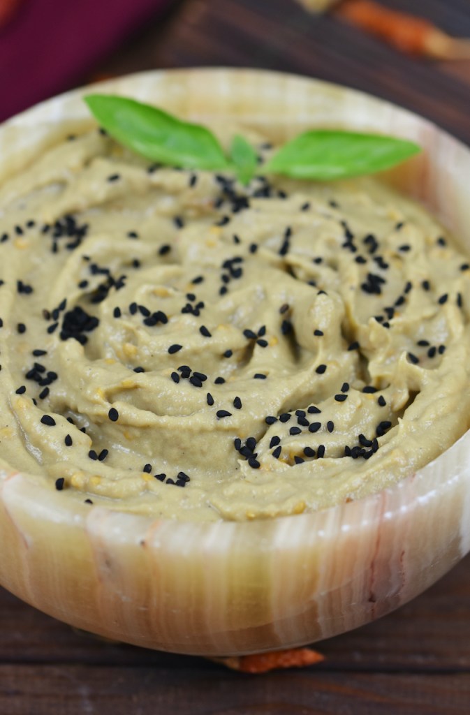 Orientalisches Mutabbal in einer Schale garniert mit Schwarzkümmelsamen und Basilikum. Hintergrund dunkel.