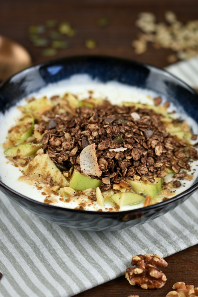 Schokoladen Granola in einer Schüssel mit Joghurt und Äpfeln.
