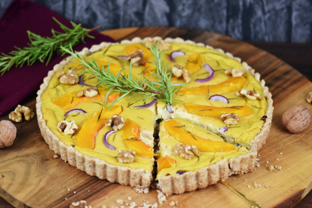 Runde Kürbis-Quiche mit Walnüssen und Rosmarin. Hintergrund dunkel.