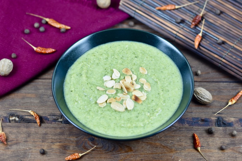 cremige Brokkolisuppe in schwarzer Schale, dekoriert mit Mandelplättchen. Hintergrund dunkel