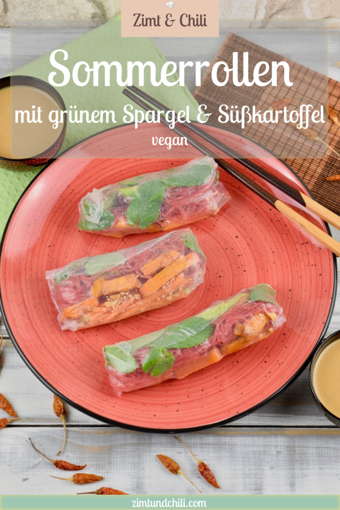 Drei Sommerrollen mit grünem Spargel und Süßkartoffel auf einem roten Teller. Auf dem Teller liegen auch Stäbchen. Im Hintergrund sieht man zwei Schälchen mit Erdnusssauce. Beschrifteter Pin.