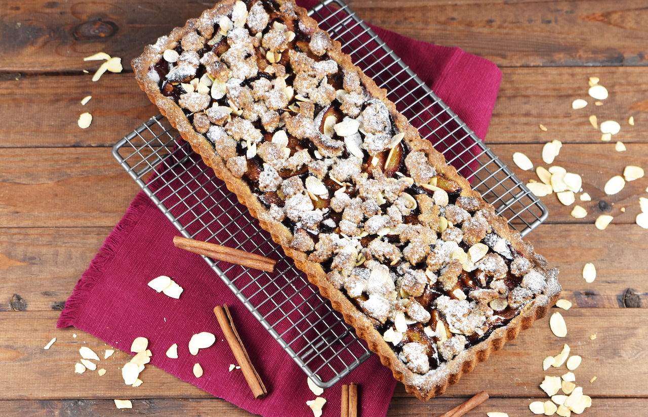 Glutenfreie Pflaumen-Tarte mit Zimtstreuseln. Hintergrund dunkel.