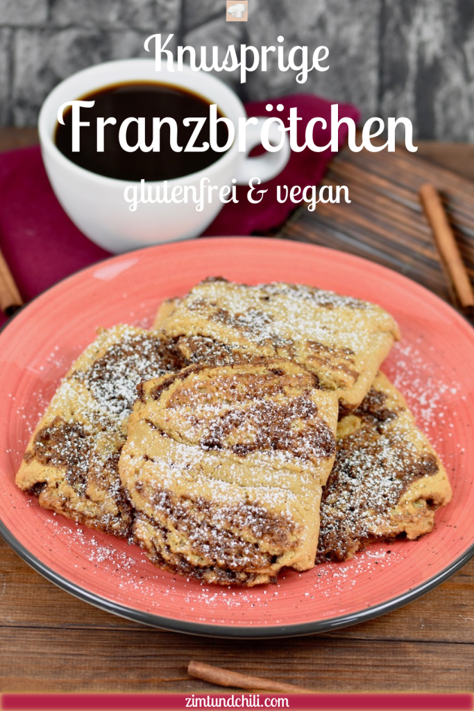 Glutenfreie Franzbrötchen auf rotem Teller. Im Hintergrund sieht man Zimtstangen, eine weiße Tasse gefüllt mit Kaffee und ein Stück von einem Nudelholz. Der Hintergrund ist dunkel. Beschriftung auf dem Bild (Knusprige Franzbrötchen vegan und glutenfrei)