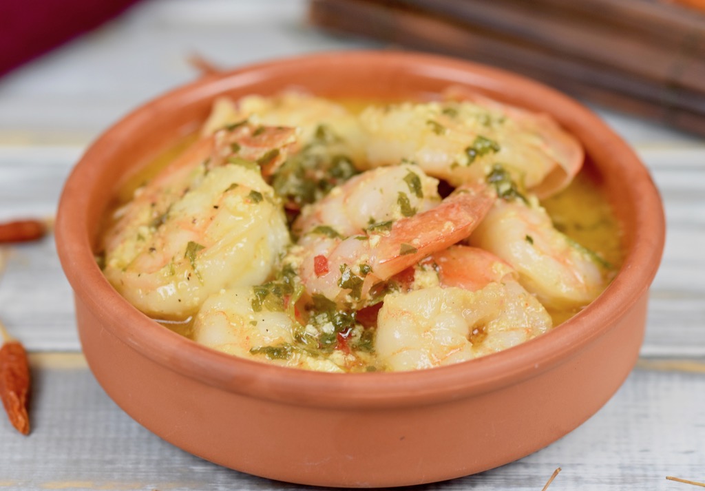 Gambas al Pil Pil in einer Knoblauch-Weißwein-Sauce in einer Tonschale. Hintergrund hell.