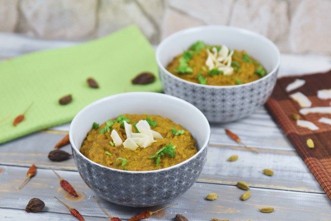 Rotes Linsen Dal in zwei Schalen, garniert mit Koriander und Kokoschips. Hintergrund hell.