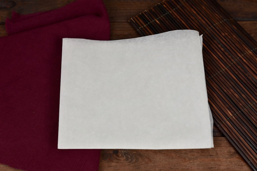 Ein Blatt weißes Backpapier 2 mal gefaltet. Hintergrund dunkel.