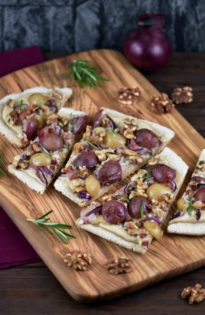 Flammkuchen mit Weintrauben und Walnüssen in Stücke geschnitten auf einem Holzbrett.