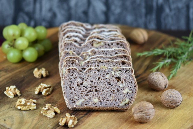 Glutenfreies Walnussbrot aufgeschnitten auf Holzbrett. Hintergrund dunkel.
