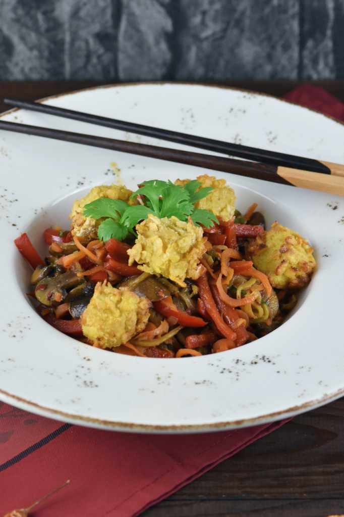 Asiatisches Wokgemüse mit knusprigem Tofu auf weißem Teller. Hintergrund dunkel.