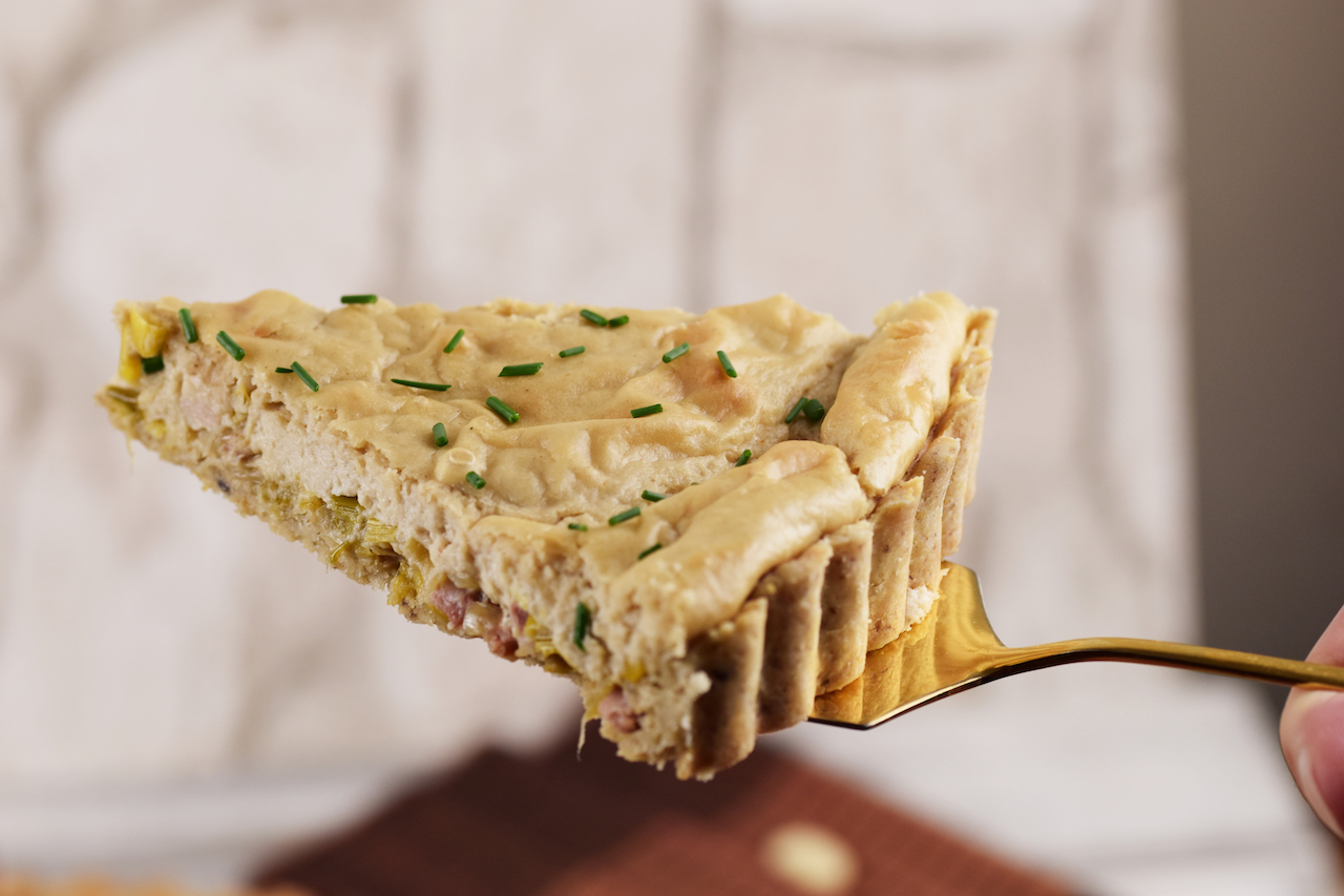 1 Stück Quiche Lorraine mit Lauch auf einem Tortenheber. Hintergrund hell.