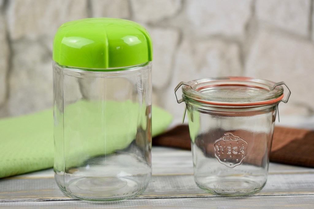 Ein Glas zum Einwecken mit Deckel und ein anderes Glas mit hellgrünem Plasikdeckel stehen vor hellem Hintergrund.