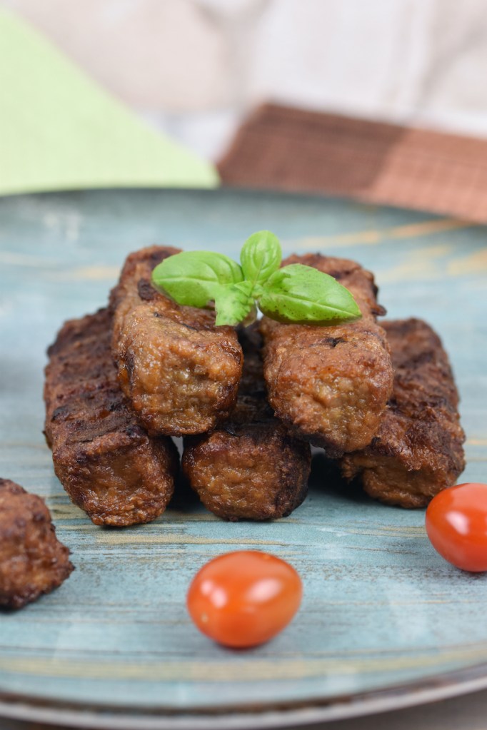 Mehrere Mici oder Mititei auf einem bläulichen Teller. Hintergrund hell.