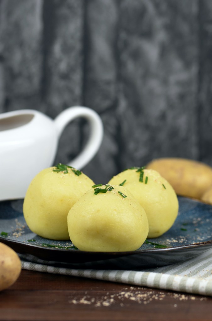 Drei Kartoffelklöße liegen auf einem auf dunkelblauem Teller.