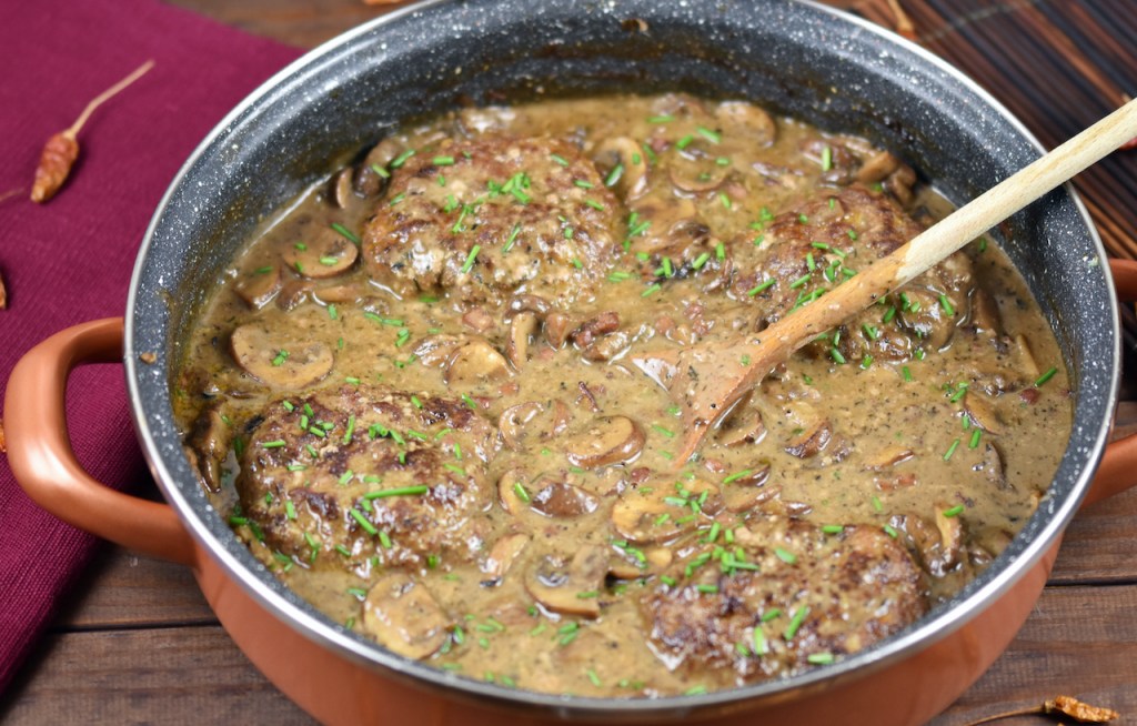 Frikadellen aus dem Backofen in cremiger Pilzsauce in einer tiefen Pfanne. Hintergrund dunkel.