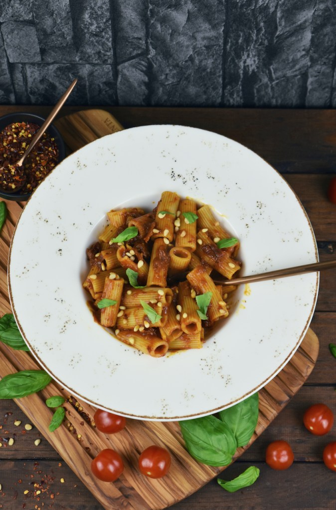 Pasta mit karamellisierten Zwiebeln auf weißem Teller. Hintergrund dunkel.