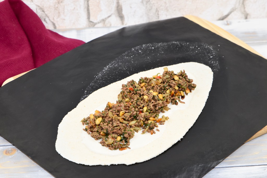 Pizzateig belegt mit der Hackfüllung.