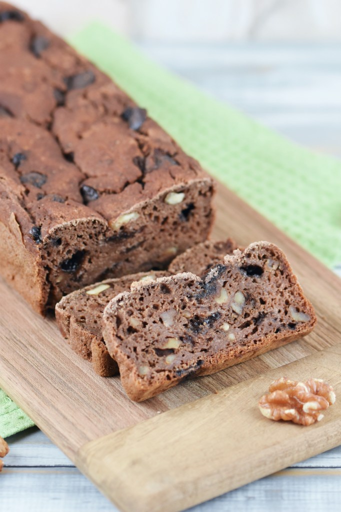 Angeschnittenes Bananenbrot mit Schokolade und Walnüssen auf Holzbrett. Hintergrund hell.