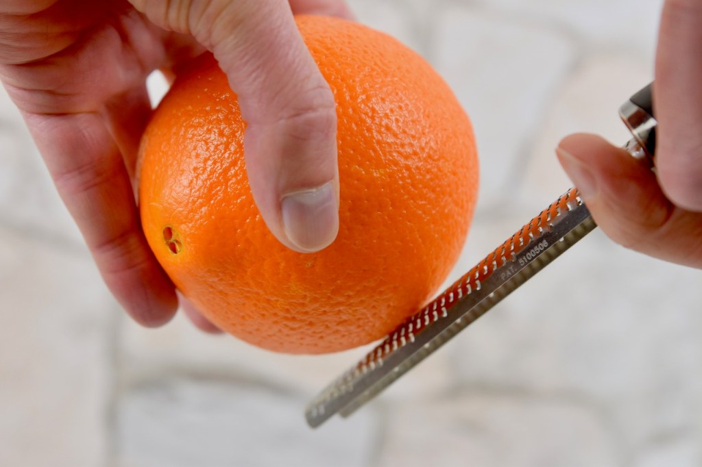 Orangenschale wird von einer Orange abgerieben. Hintergrund hell.