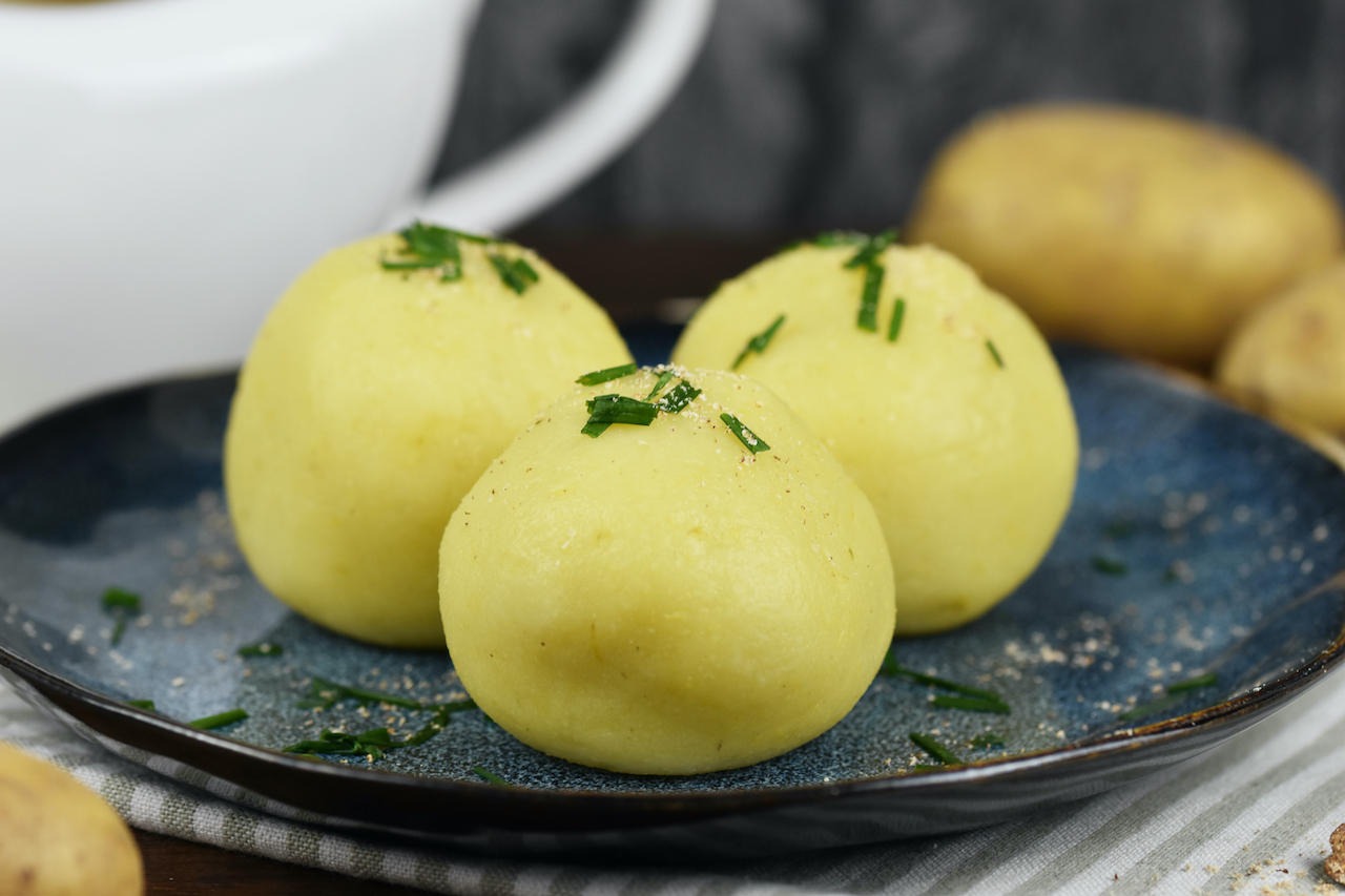 Drei Kartoffelklöße liegen auf einem auf dunkelblauem Teller.