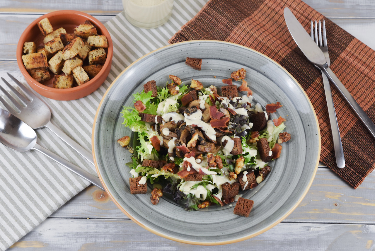 Veganer Caesar Salad mit Pilzen und Walnüssen auf grauem Teller. Hintergrund hell.