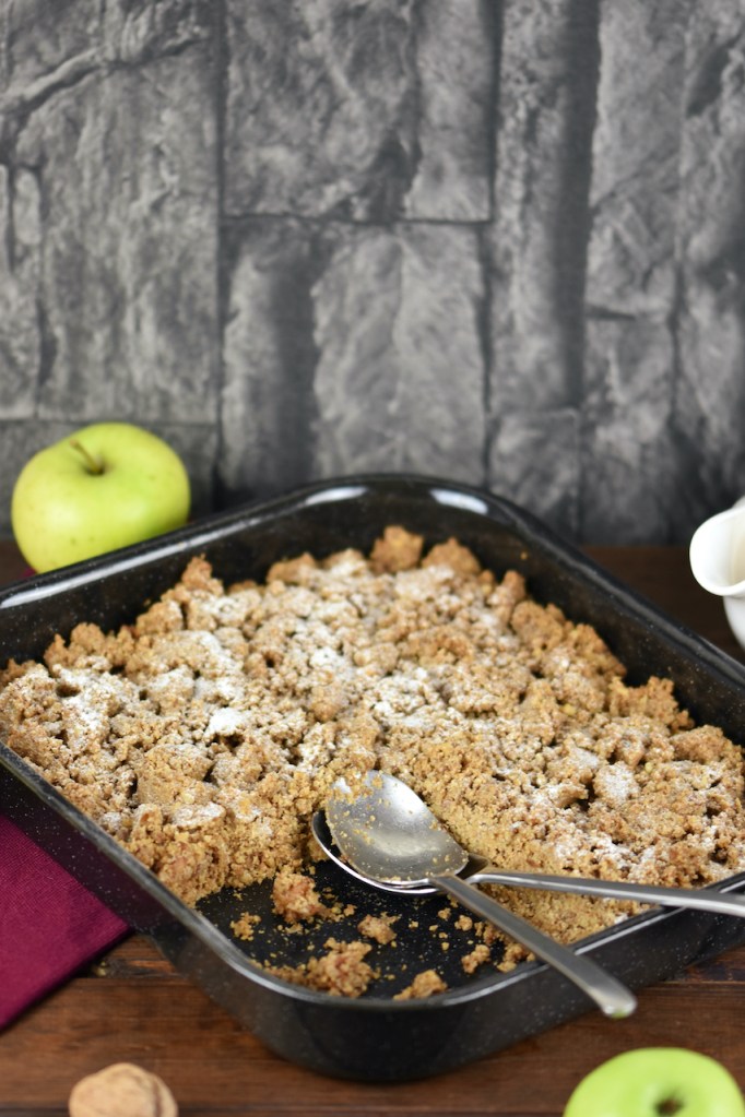 Apple Crumble mit Walnüssen und Haferflocken in einer Auflaufform. Hintergrund dunkel.