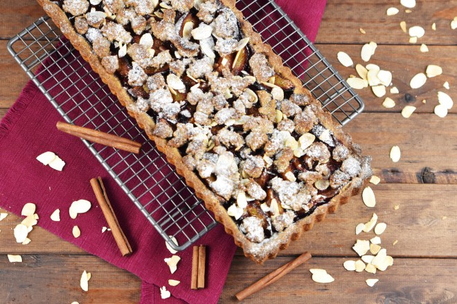 Glutenfreie Pflaumen-Tarte mit Zimtstreuseln. Hintergrund dunkel.