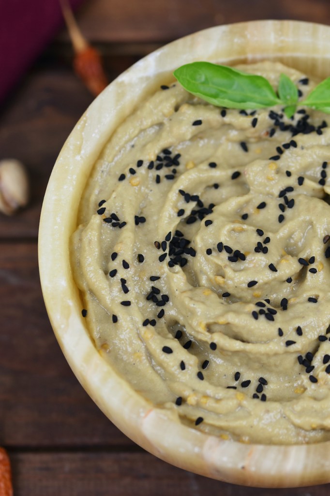 Orientalisches Mutabbal in einer Schale garniert mit Schwarzkümmelsamen und Basilikum. Hintergrund dunkel.
