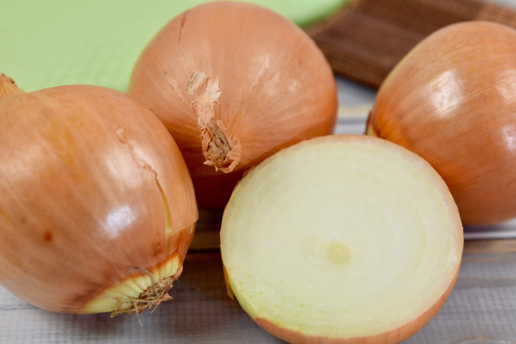 drei gelbe Zwiebeln und eine aufgeschnittene Hälfte, Hintergrund hell