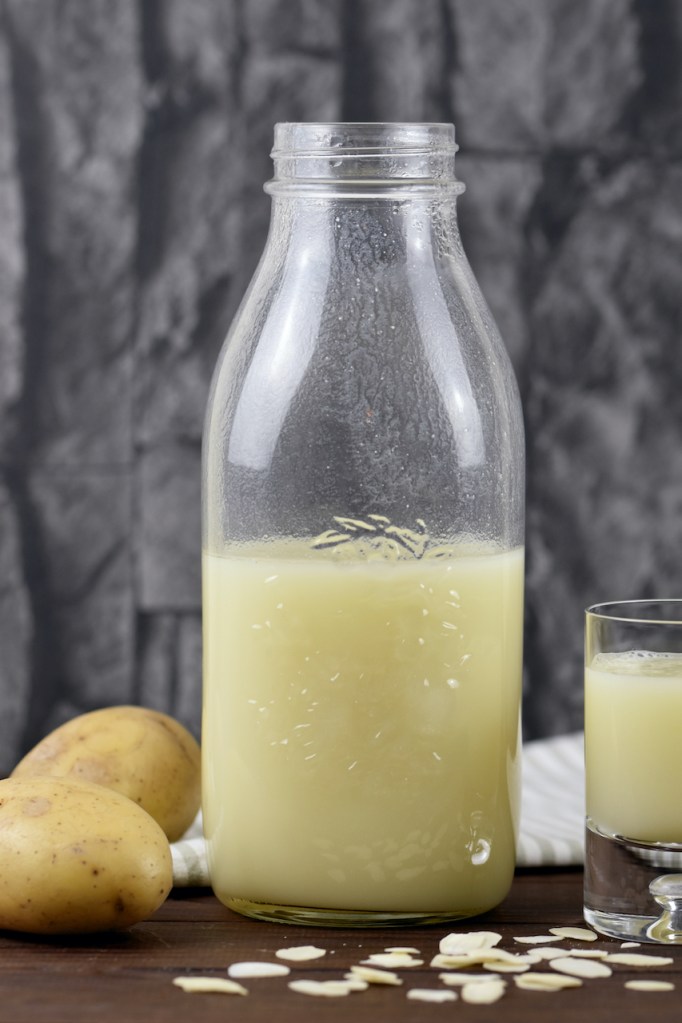 Vegane Milch aus Kartoffeln in einer Glasflasche und einem Glas. Hintergrund dunkel.