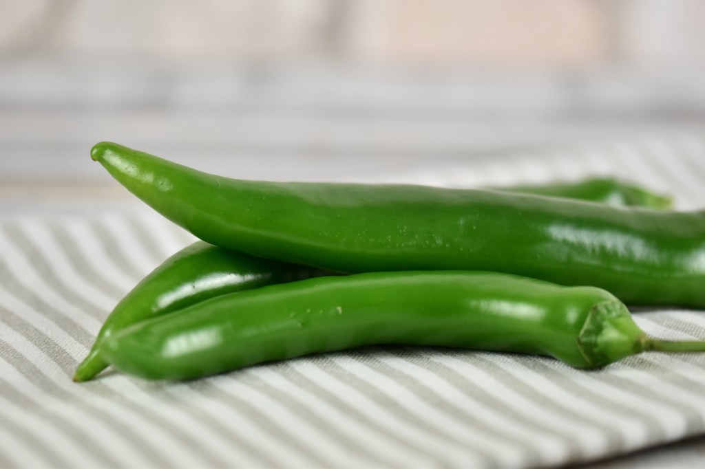 Drei grüne Chilis auf heller gestreifter Stoffserviette.