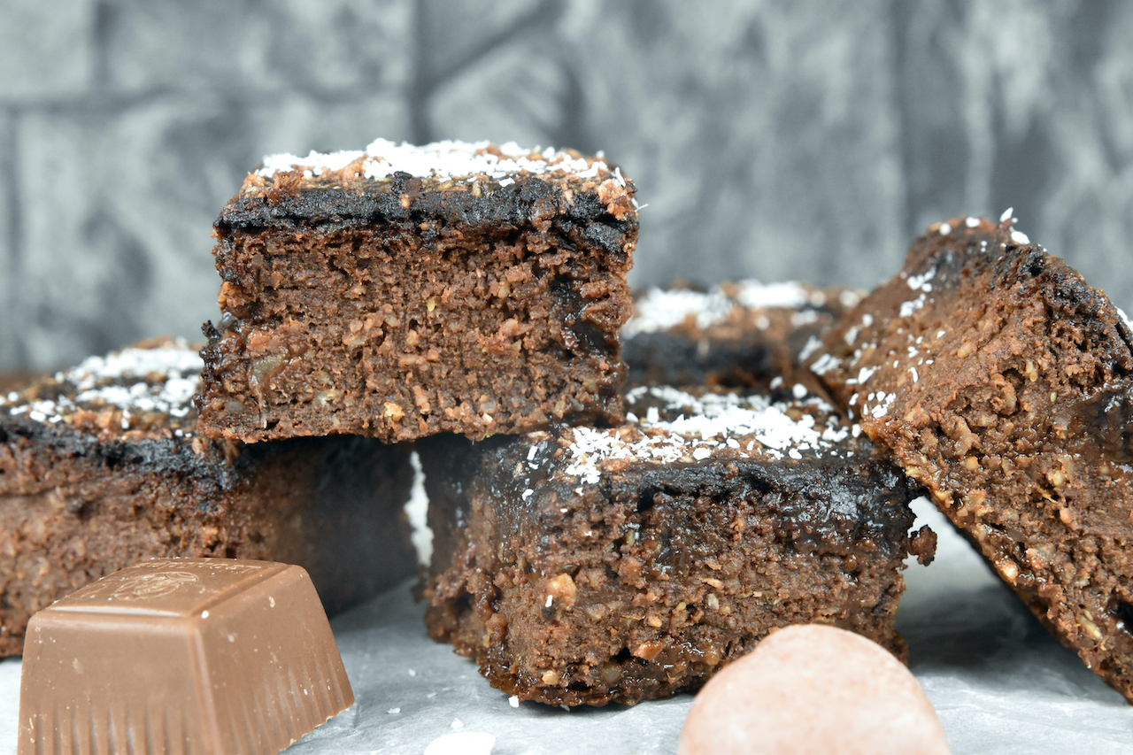 Vegane Brownies übereinander gestapelt auf Backpapier. Hintergrund dunkel.
