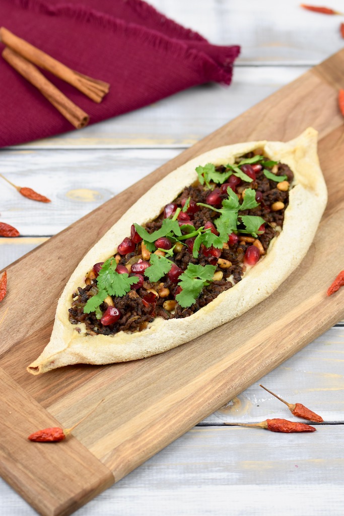 Pide mit Zimt-Hackfleisch, garniert mit Koriandergrün, auf einem Holzbrett.