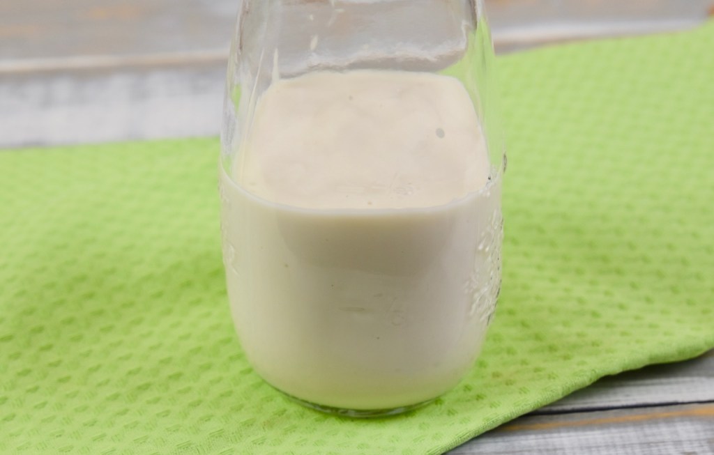 pflanzliche Sahne in einer kleinen Glasflasche. Hintergrund hellgrün.